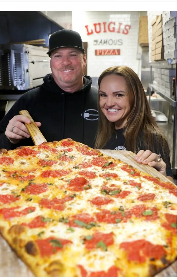 A man and woman sitting next to a large pizza.